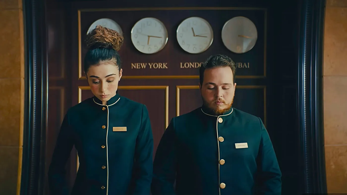 Two hotel receptionists in navy uniforms under a row of world clocks, Hilton commercial with music by Santiago Bianchi